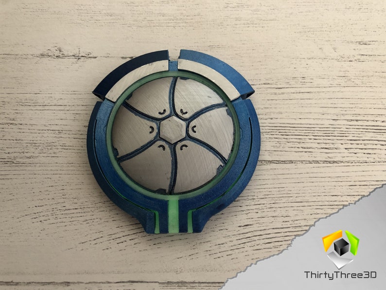 May include: A 3D printed, blue, green, and white circular object with a geometric design. The object has a raised center with a hexagonal pattern.
