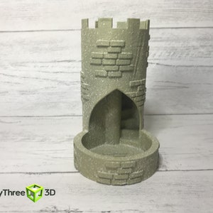 May include: A gray stone tower-shaped dice tower with a brick pattern and a rounded base. The tower has a small archway opening on one side.