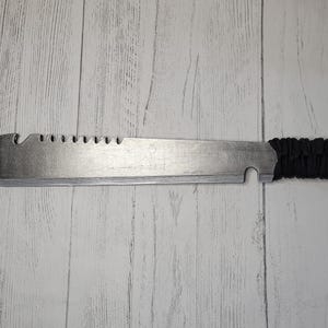 Peut inclure: Une machette argent&eacute;e avec une poign&eacute;e en paracorde noire. La lame est dentel&eacute;e et comporte un petit trou pr&egrave;s de la poign&eacute;e.