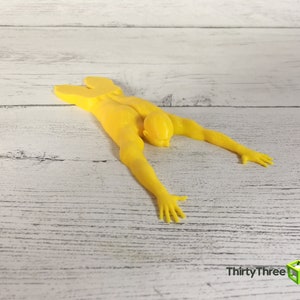 May include: A yellow 3D printed doorstop shaped like a person lying face down with arms outstretched.