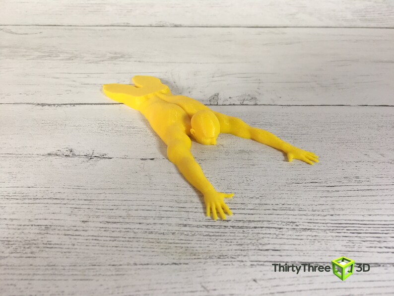 May include: A yellow 3D printed doorstop shaped like a person lying face down with arms outstretched.