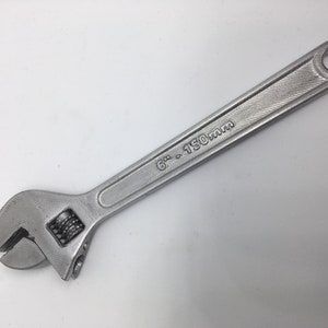 Puede incluir: Una llave inglesa de plata con una medida de 6 pulgadas a 150 mm marcada en el mango.