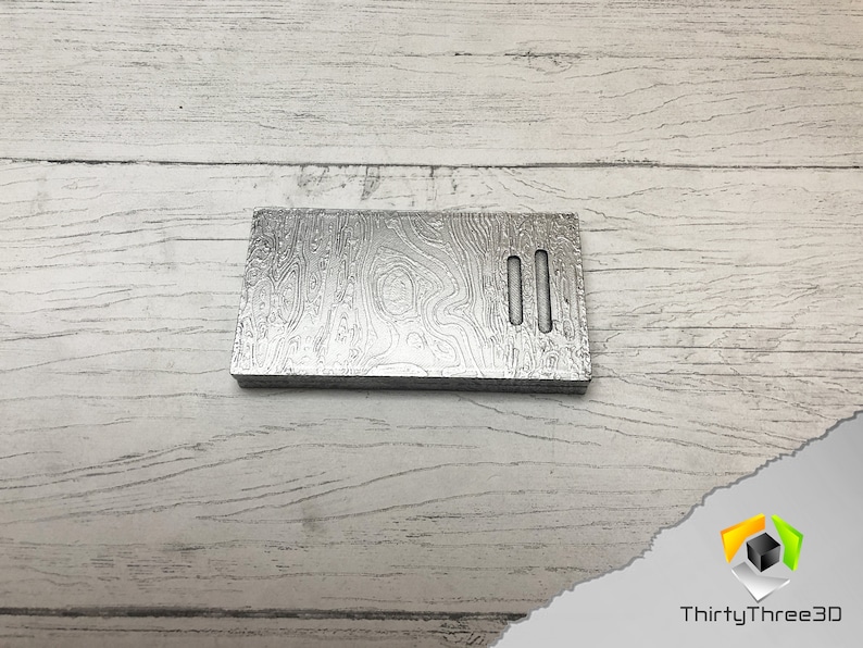 May include: A silver metal plate with a wood grain pattern and two rectangular cutouts. The plate is on a white wooden surface.