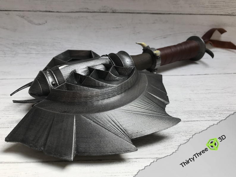 May include: A 3D printed, black metal axe with a detailed, textured design. The axe has a long handle with a brown leather wrap and a metal cap. The axe head is shaped like a crescent moon with a sharp edge.