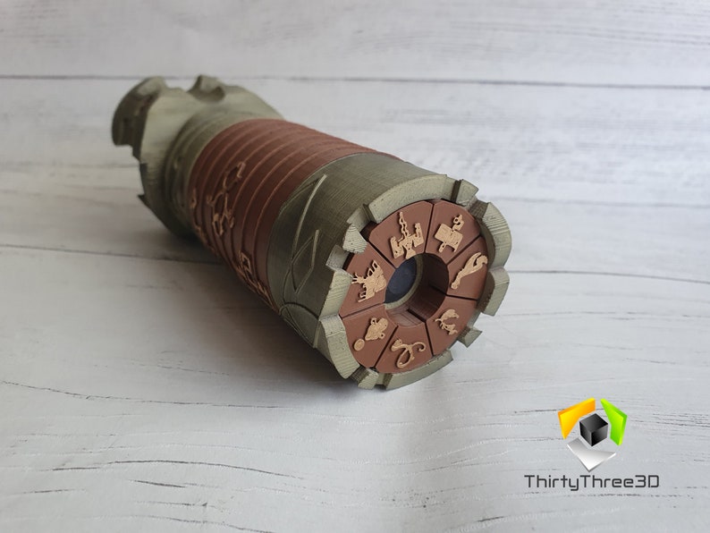 May include: A brown and green wooden kaleidoscope with a circular viewing end. The end is decorated with a brown circle with various symbols and designs.