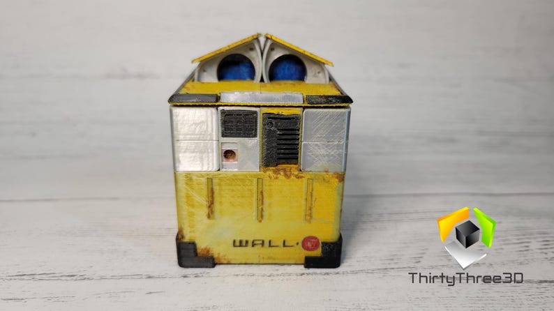 May include: A yellow and silver WALL-E robot toy with a rusty finish. The robot has a rectangular body with a small, square head and two blue eyes. The robot is standing on a white wooden surface.