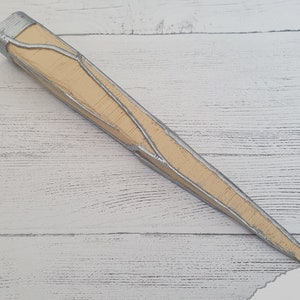 Op de afbeelding: Een lang, puntig, houten voorwerp met een zilveren metallic afwerking. Het voorwerp heeft een getextureerd oppervlak en een puntige punt.
