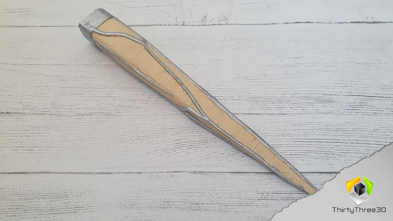 Op de afbeelding: Een lang, puntig, houten voorwerp met een zilveren metallic afwerking. Het voorwerp heeft een getextureerd oppervlak en een puntige punt.