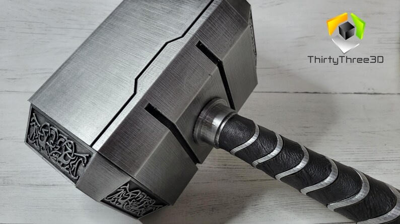 May include: A silver-colored hammer with a black and silver handle. The hammer head has a detailed design and the handle has a textured grip.