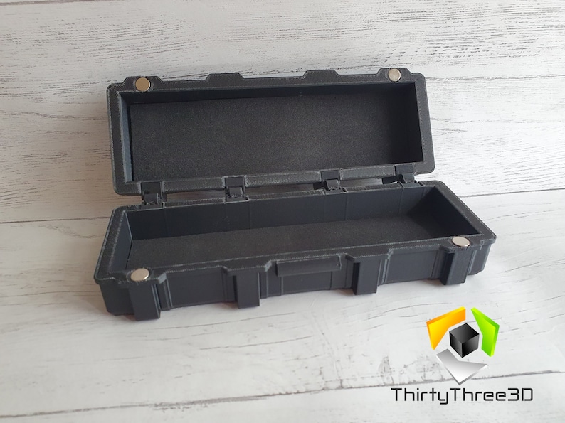 May include: A black plastic storage case with a hinged lid and a latch. The case is empty and has a textured surface.
