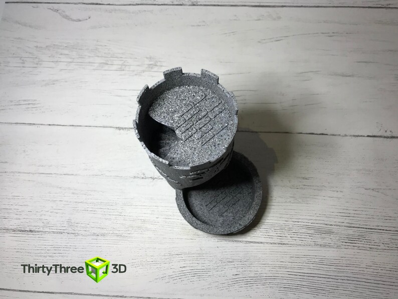 May include: A gray 3D printed tower with a crenellated top and a textured surface. The tower is in two pieces, with the top piece sitting on the bottom piece.