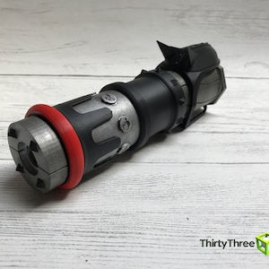 May include: A detailed, 3D-printed object with a cylindrical design. It features a silver-colored body with black and red accents, including a red ring and black components. The object has a complex, mechanical appearance.