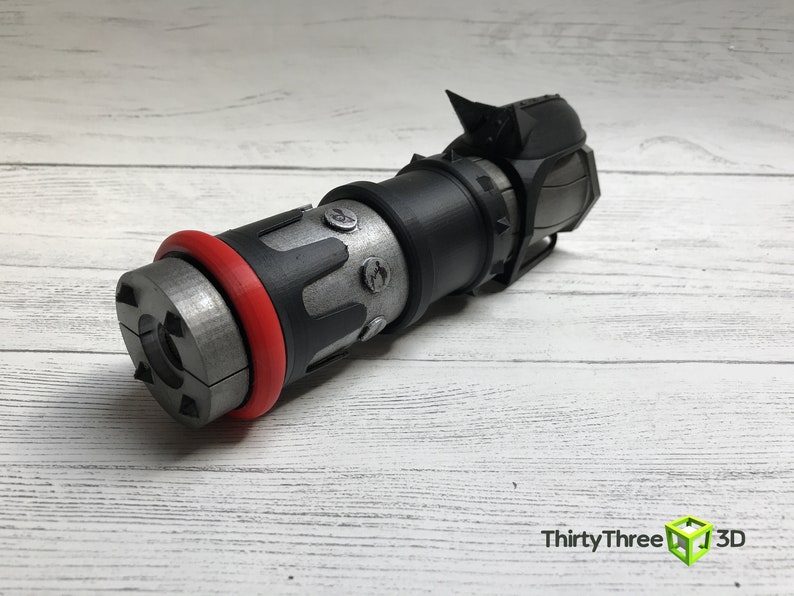 May include: A detailed, 3D-printed object with a cylindrical design. It features a silver-colored body with black and red accents, including a red ring and black components. The object has a complex, mechanical appearance.