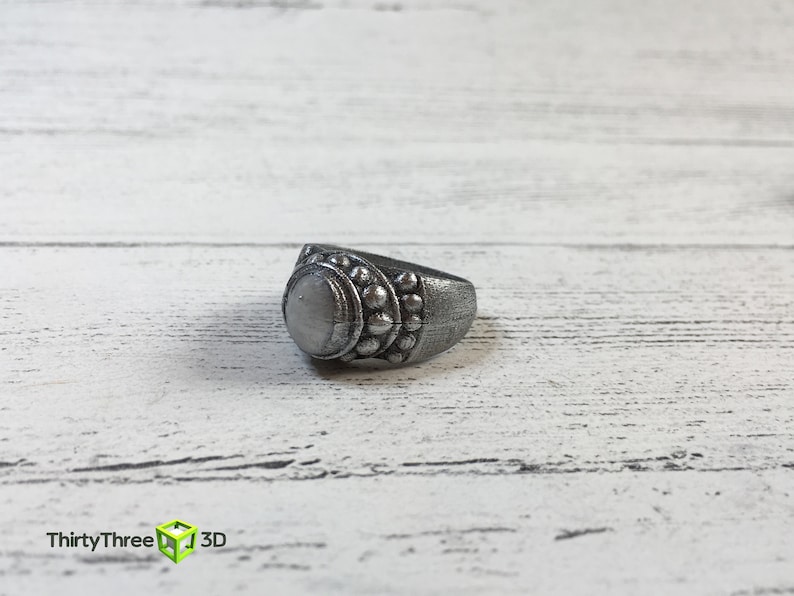 May include: A silver ring with a round, white stone and a decorative band of small, raised circles.