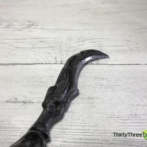May include: A black, curved object with a pointed tip, possibly a decorative element or prop. The object has intricate detailing and a textured surface. The background is a light-colored wooden surface. The text "ThirtyThree 3D" is visible in the lower right corner.