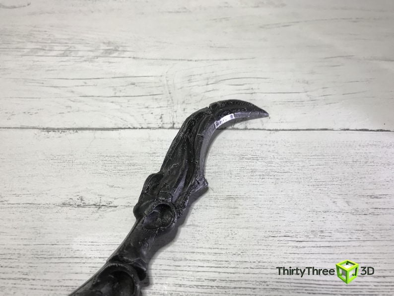 May include: A black, curved object with a pointed tip, possibly a decorative element or prop. The object has intricate detailing and a textured surface. The background is a light-colored wooden surface. The text "ThirtyThree 3D" is visible in the lower right corner.