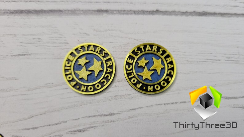 Puede incluir: Dos pines de metal de color dorado con las palabras "Stars Raccoon Police" y tres estrellas doradas sobre fondo azul.