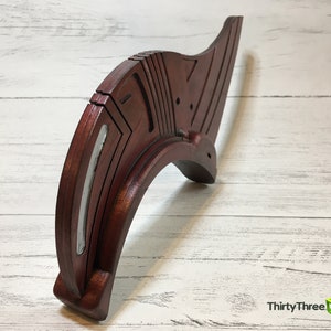 May include: A wooden, curved, decorative piece with a silver accent. The piece is made of multiple layers of wood and has a geometric design.