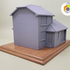 May include: A gray 3D printed model of a house with a wooden base. The house has a pitched roof, two windows, and a door.