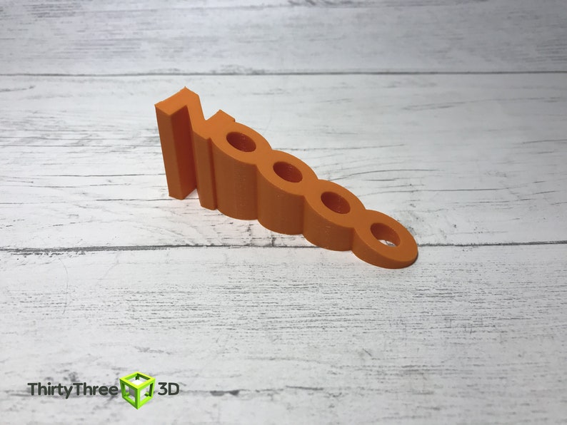 May include: Orange plastic doorstop shaped like the number 10000. The doorstop is on a white wooden surface.