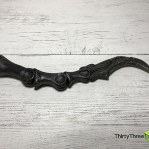 May include: A black, claw-shaped prop, possibly for cosplay or decoration, rests on a white wooden surface. The prop has a detailed, textured surface and a curved, pointed end. The text "ThirtyThree 3D" is visible.