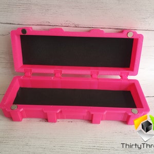 May include: A bright pink rectangular box with a black foam interior. The box has a hinged lid and magnetic closures. The box is open and the lid is propped up.