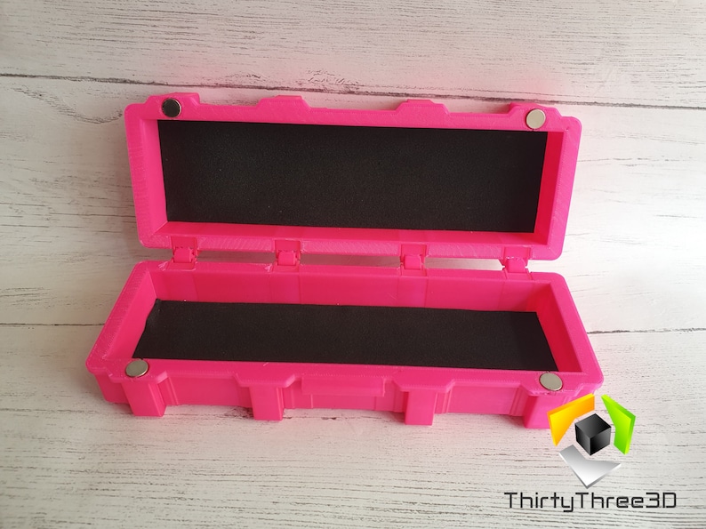 May include: A bright pink rectangular box with a black foam interior. The box has a hinged lid and magnetic closures. The box is open and the lid is propped up.