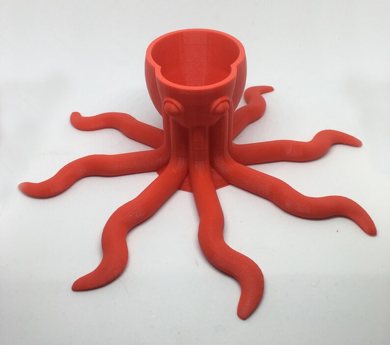 May include: A bright orange octopus-shaped ceramic holder with a cup-like top. The holder has eight tentacles.