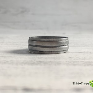May include: A silver ring with three horizontal bands. The ring is made of metal and has a brushed finish.