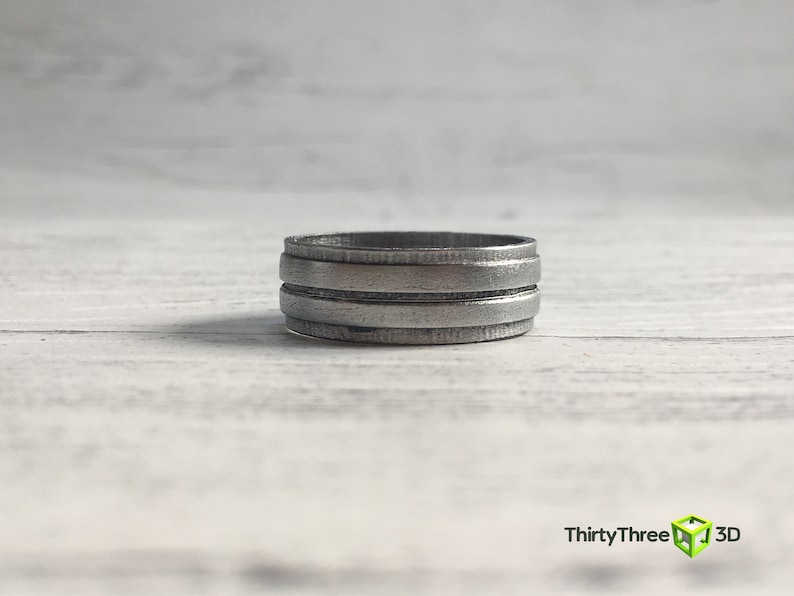 May include: A silver ring with three horizontal bands. The ring is made of metal and has a brushed finish.