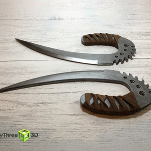 May include: Two silver-colored, curved, and serrated knives with brown leather handles. The knives are on a white wooden surface.