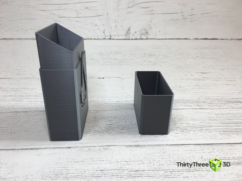 May include: Two gray 3D printed boxes, one tall and narrow, the other short and wide. The tall box has a design on the front.