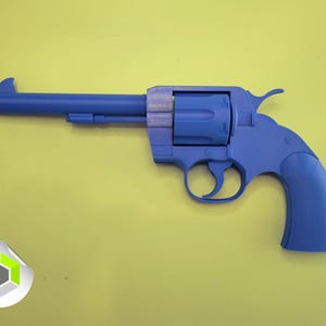 May include: A blue toy revolver with an orange tip, set against a yellow background. The toy gun features a detailed design, including a cylinder, trigger, and grip, and is likely a prop or collectible item.