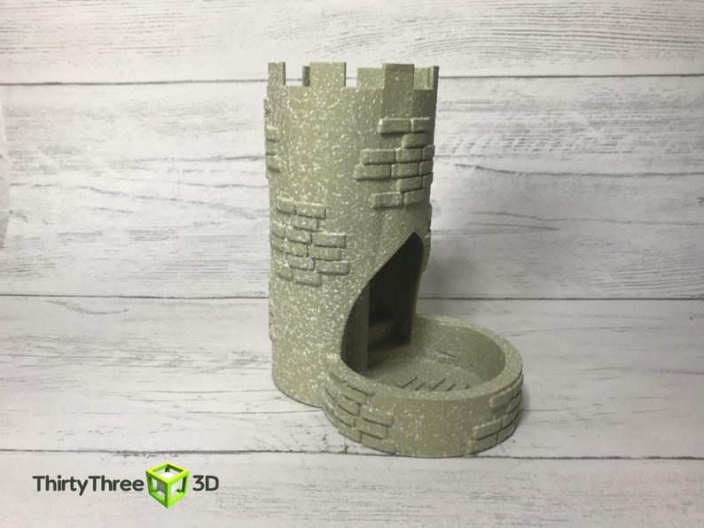 May include: A gray stone tower-shaped dice rolling tower with a rounded base. The tower has a small opening at the top and a larger opening at the base.