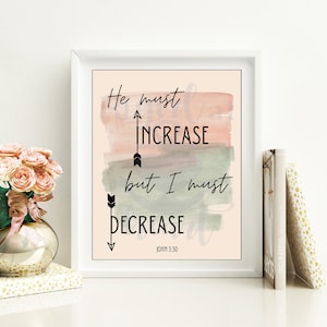 May include: A white framed print with a watercolour background in shades of pink and green. The print features the text "He must increase but I must decrease" with arrows pointing up and down. The text "John 3:30" is at the bottom of the print.