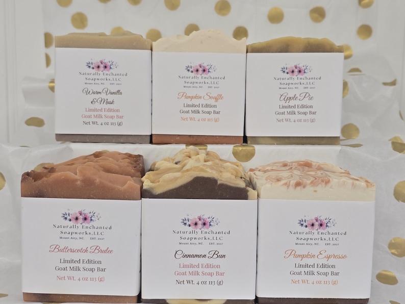 May include: Six rectangular goat milk soap bars arranged in two rows. Each bar features a white paper label with the Naturally Enchanted Soapworks logo, scent name, and a net weight of 4 oz (113 g). Scents include Warm Vanilla & Musk, Pumpkin Souffle, Apple Pie, Butterscotch Brulee, Cinnamon Bun, and Pumpkin Espresso.