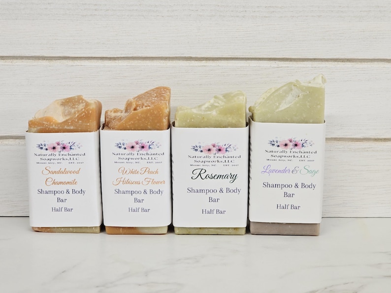 K&ouml;nnte beinhalten: Vier halbe Shampoo- und K&ouml;rperseifen in wei&szlig;er Papierverpackung. Die Seifen sind mit den D&uuml;ften Sandelholz Kamille, White Peach Hibiscus Flower, Rosmarin und Lavendel & Salbei beschriftet. Die Verpackung hat ein Blumenmuster.