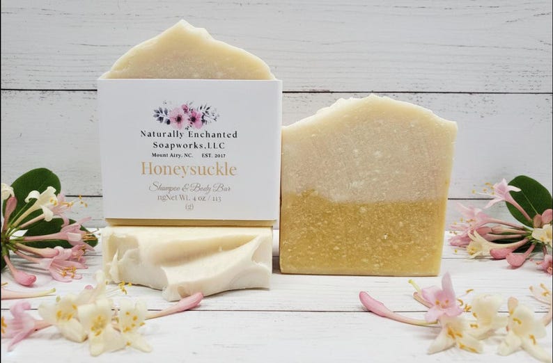 K&ouml;nnte beinhalten: Zweifarbige Honeysuckle Shampoo- und K&ouml;rperseifen mit einer wei&szlig;en Schachtel mit floralen Akzenten und Text. Die Seifen wiegen jeweils 113 g. Rosa und wei&szlig;e Blumen sind um die Seifen auf einer wei&szlig;en Holzoberfl&auml;che verstreut.