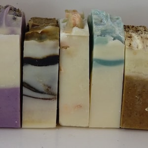 May include: A row of 12 different colored bars of soap. The soaps are arranged in a row from left to right. The soaps are all different colors and have different patterns.