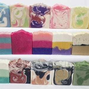 May include: A collection of rectangular bars of soap arranged in three rows. The bars feature various designs including solid color blocks, marbled swirls, and layered patterns in a wide range of colors such as blue, pink, purple, yellow, green, and black.