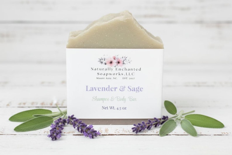 K&ouml;nnte beinhalten: Ein hellgr&uuml;nes Shampoo- und K&ouml;rperseifenst&uuml;ck mit dem Text "Lavender & Sage" und "Net Wt. 4.5 oz." Die Seife wird mit Zweigen von Lavendel und Salbei pr&auml;sentiert. Das Produkt stammt von Naturally Enchanted Soapworks, LLC.