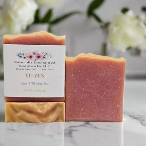 May include: A rectangular bar of pink goat milk soap with a textured top, wrapped in a white paper label featuring floral graphics and the text Naturally Enchanted Soapworks, L.L.C, Mount Airy, NC, EST. 2017, YU-ZEN, Goat Milk Soap Bar, Net Wt. 4 oz.