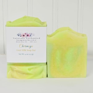 May include: Two bars of light yellow and green goat milk soap. One bar is wrapped in a white paper label with the text Naturally Enchanted Soapworks, LLC, Mount Airy, NC, Est 2017, Cherimoya, Goat Milk Soap Bar, Net Wt. 4 oz 113 g.