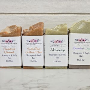 K&ouml;nnte beinhalten: Vier halbgro&szlig;e Shampoo- und K&ouml;rperseifen in wei&szlig;er Verpackung. Die Seifen sind mit den D&uuml;ften Sandelholz Kamille, White Peach Hibiscus Flower, Rosmarin und Lavendel & Salbei beschriftet. Jede Seife hat eine einzigartige Farbe und Textur.