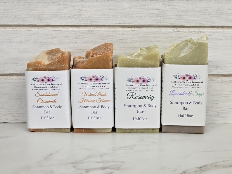 K&ouml;nnte beinhalten: Vier halbgro&szlig;e Shampoo- und K&ouml;rperseifen in wei&szlig;er Verpackung. Die Seifen sind mit den D&uuml;ften Sandelholz Kamille, White Peach Hibiscus Flower, Rosmarin und Lavendel & Salbei beschriftet. Jede Seife hat eine einzigartige Farbe und Textur.