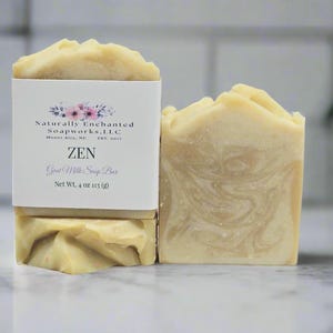 May include: A rectangular bar of beige goat milk soap with a marbled texture and a textured top. A white paper label wraps around the soap, featuring the text Naturally Enchanted Soapworks, LLC, ZEN, Goat Milk Soap Bar, and Net Wt. 4 oz.