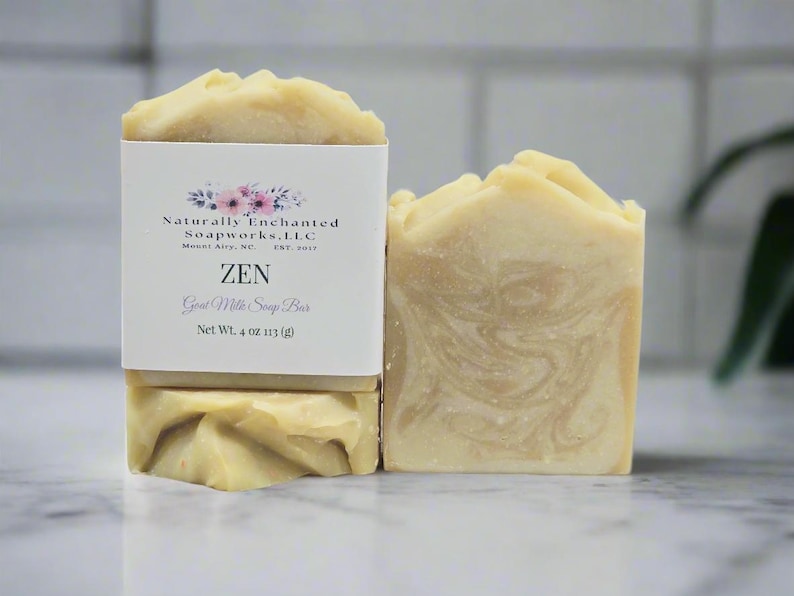 May include: A rectangular bar of beige goat milk soap with a marbled texture and a textured top. A white paper label wraps around the soap, featuring the text Naturally Enchanted Soapworks, LLC, ZEN, Goat Milk Soap Bar, and Net Wt. 4 oz.
