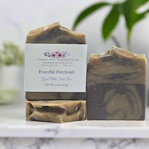 May include: Two bars of Peaceful Patchouli goat milk soap with a marbled brown and dark gray swirl pattern. One bar is wrapped in a white paper label featuring floral graphics and the text Naturally Enchanted Soapworks, LLC, Net Wt. 4 oz.
