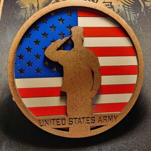 May include: Wooden circular emblem featuring the American flag with a saluting soldier silhouette. The flag design includes red and white stripes and a blue field with stars. The words "UNITED STATES ARMY" are at the bottom.