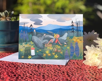May include: A greeting card featuring a colorful illustration of a girl lying on a wolf in a field of flowers. The background shows a mountain range and a blue sky with clouds.